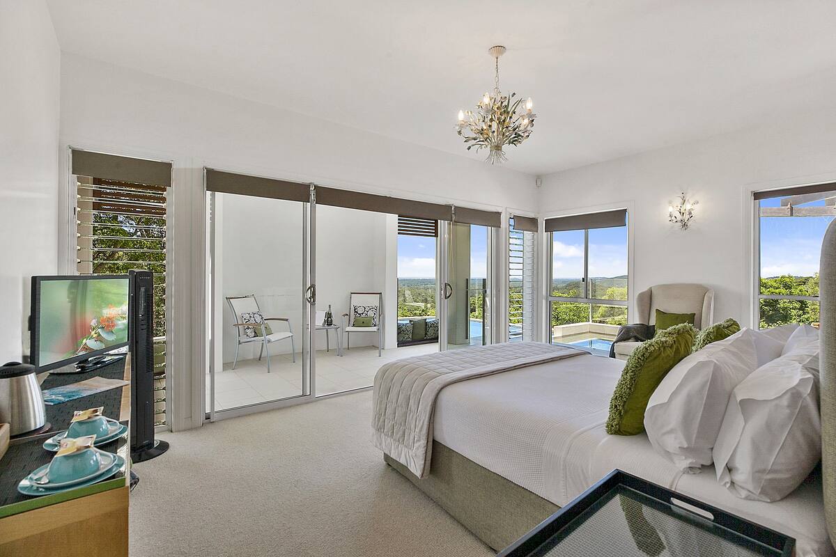 A modern bedroom with a large bed, a television, and a balcony with a view.