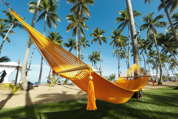 A hammock on a grassy area with palm trees in the background.