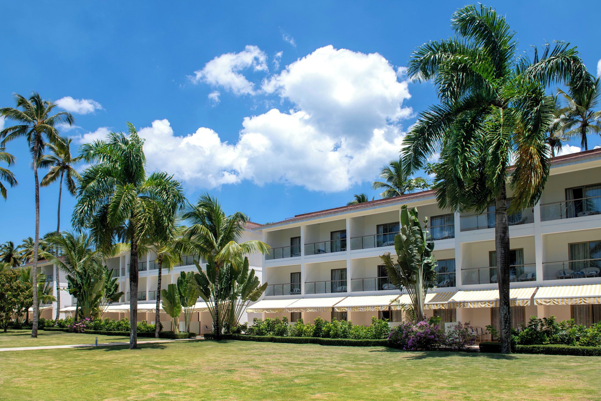 A hotel with multiple balconies, palm trees, and a clear blue sky.