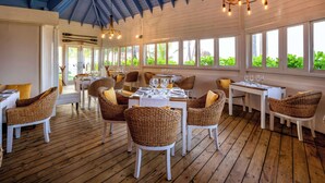 Un restaurant avec des planchers en bois et des meubles blancs, de grandes fenêtres donnant sur un espace verdoyant et un plafond bleu.