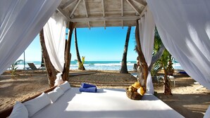 Un cabanon de plage avec un lit, des rideaux blancs et une vue sur l’océan.