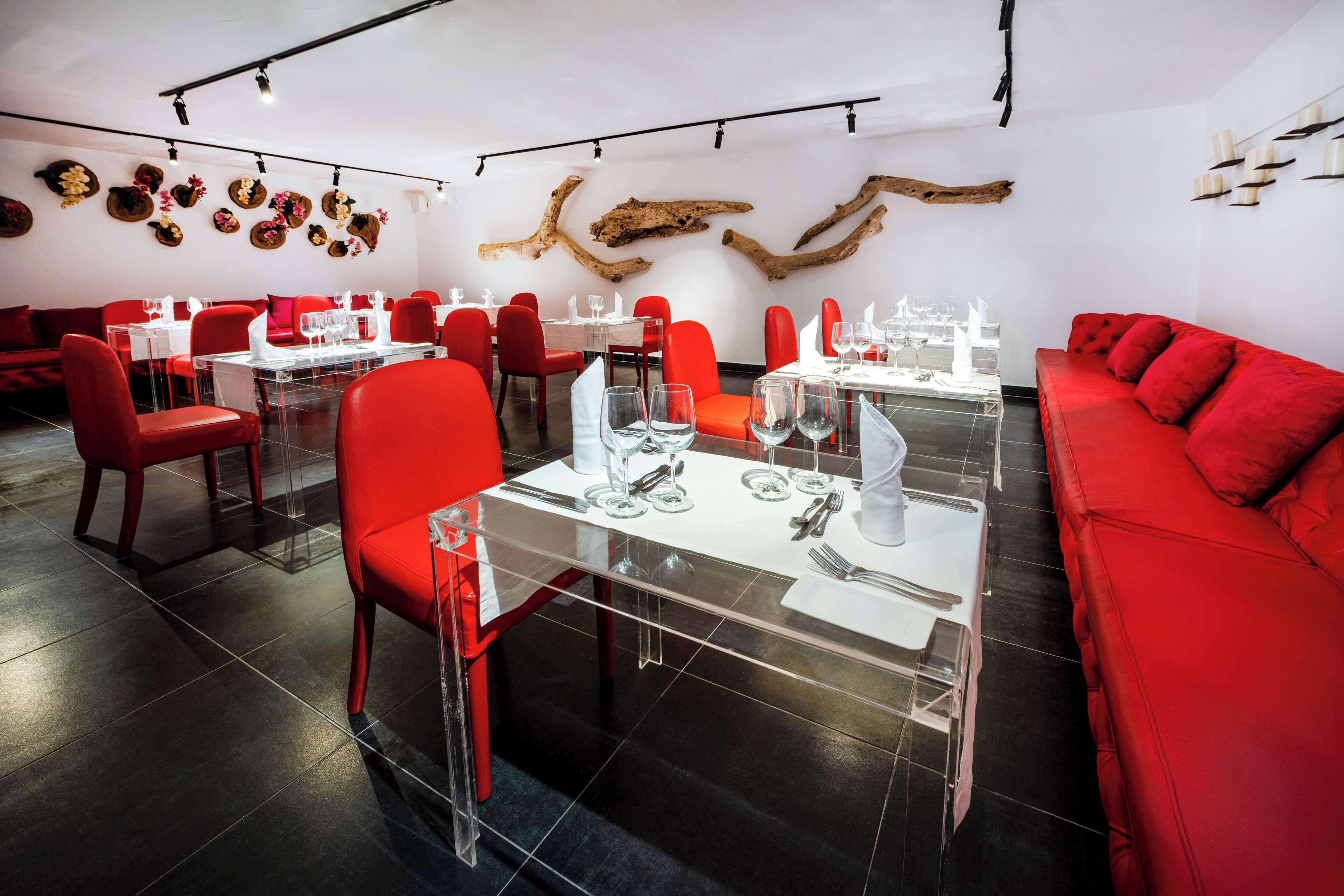 A restaurant with red chairs and tables, clear glass partitions, and decorative wall art.