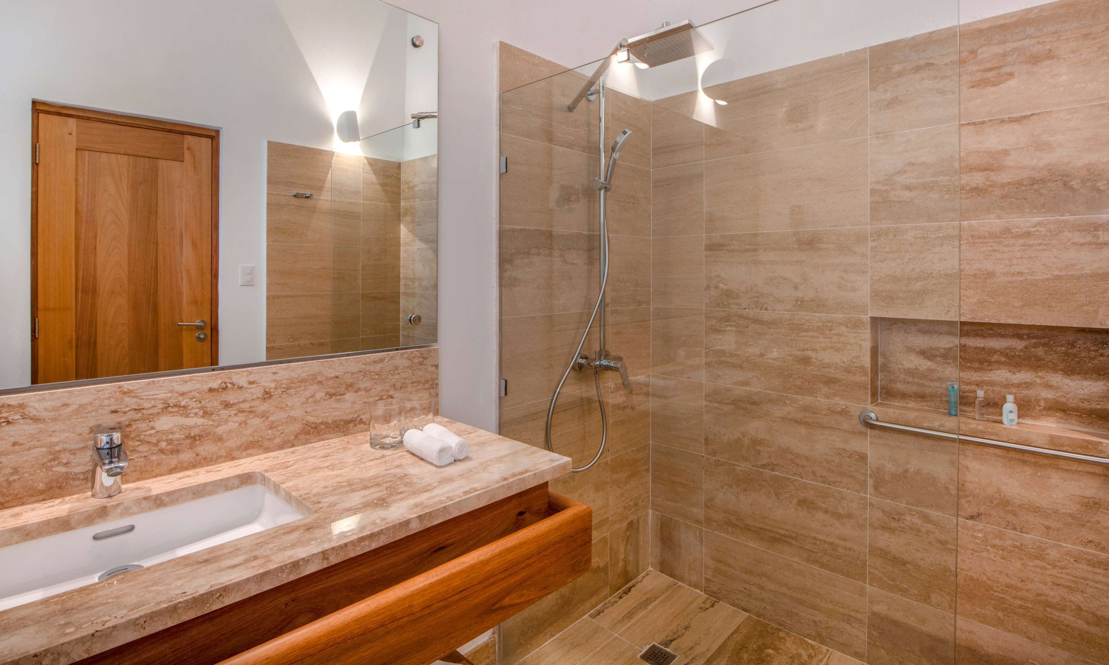 Un baño moderno con lavamanos de mármol, ducha con cerramiento de vidrio y tocador de madera.