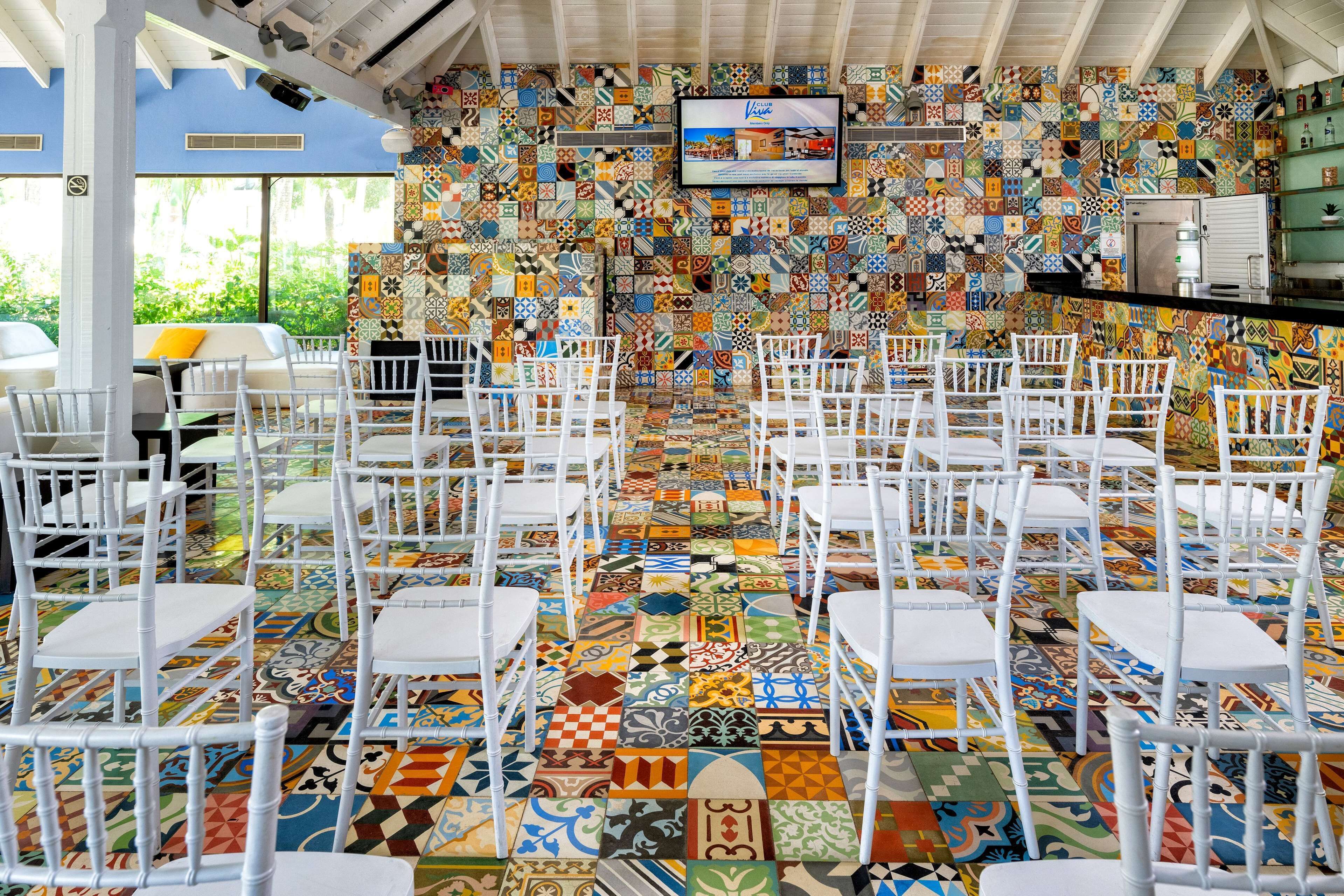 A room with a tiled floor and walls, white chairs arranged in rows, and a television mounted on the wall.