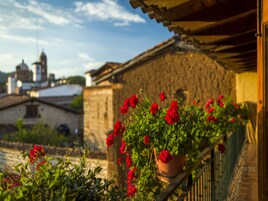 Un balcón con flores rojas, un muro de piedra y vistas a un paisaje urbano con una torre.