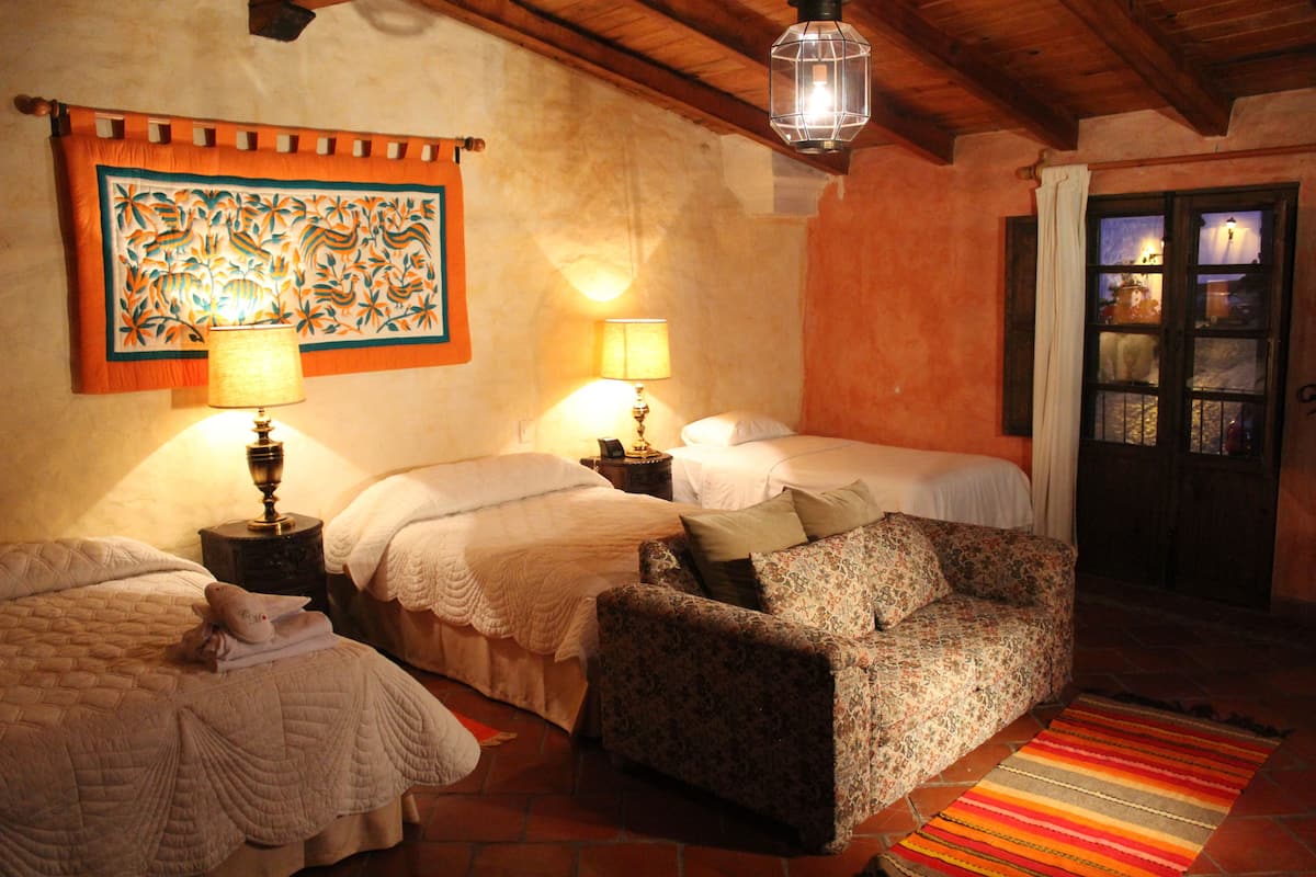 A cozy room with two beds, a patterned armchair, and a colorful rug.