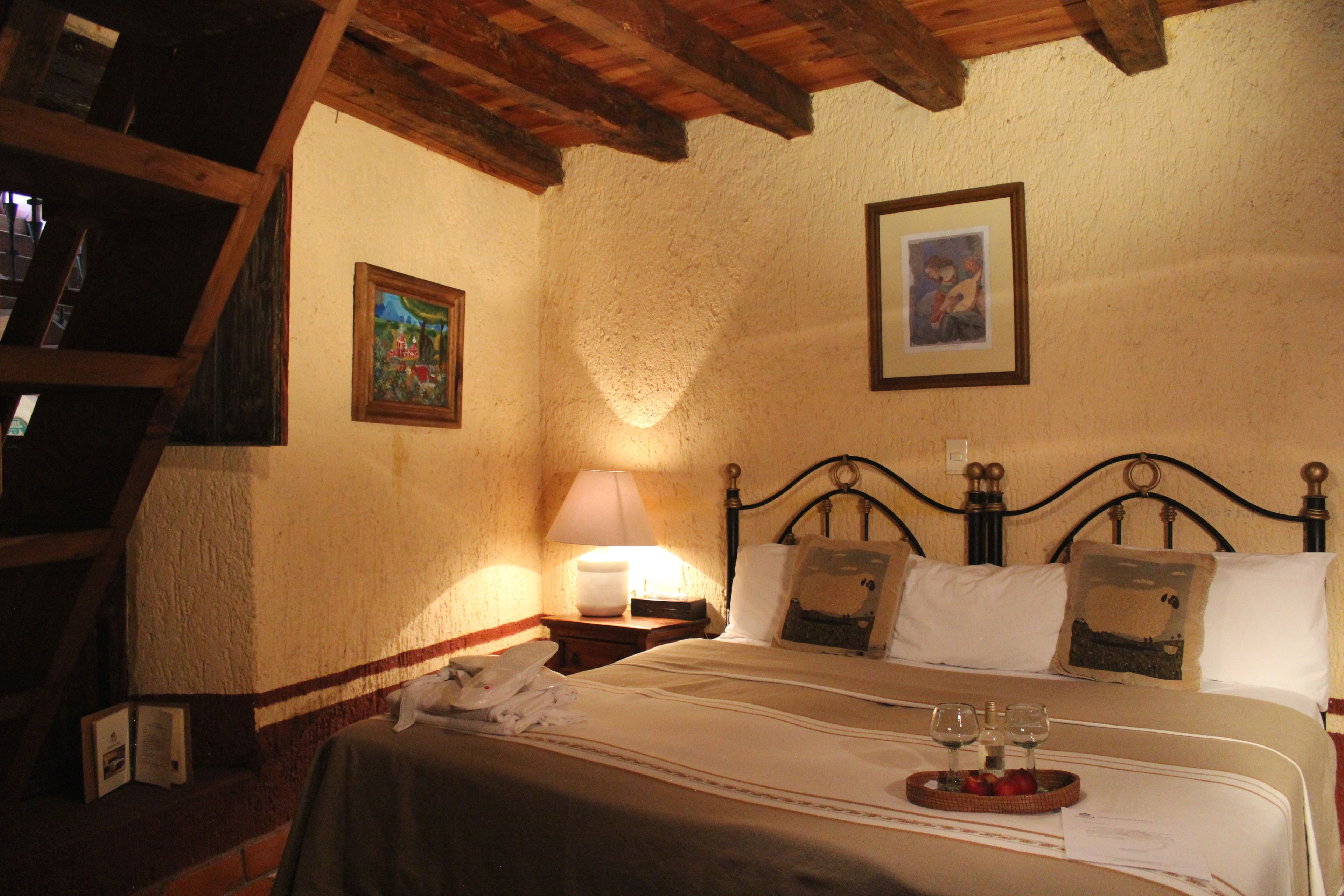 A bedroom with a wooden ceiling, a bed with white linens, two pillows, a bedside table with a lamp, and a framed picture on the wall.