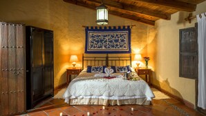 Un dormitorio con cama, dos mesitas de noche, un armario de madera, un tapiz colgante y suelo de baldosas.