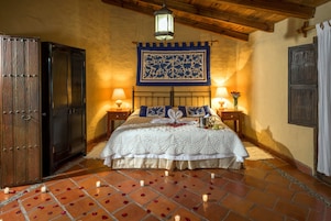 Un dormitorio con cama, dos mesitas de noche, un armario de madera, un tapiz colgante y suelo de baldosas.