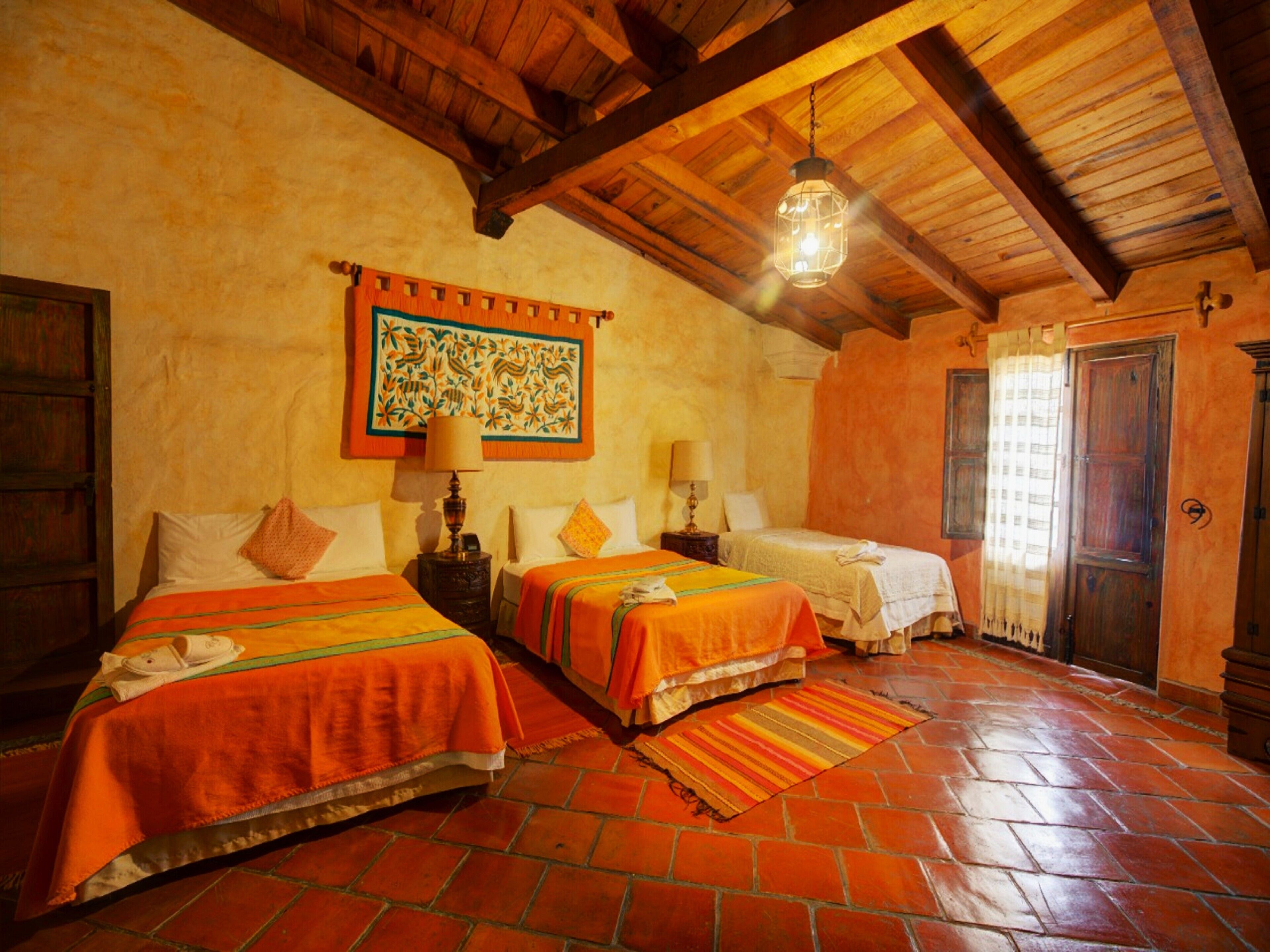 A room with two beds, a wooden ceiling, a patterned tapestry, and a tiled floor.