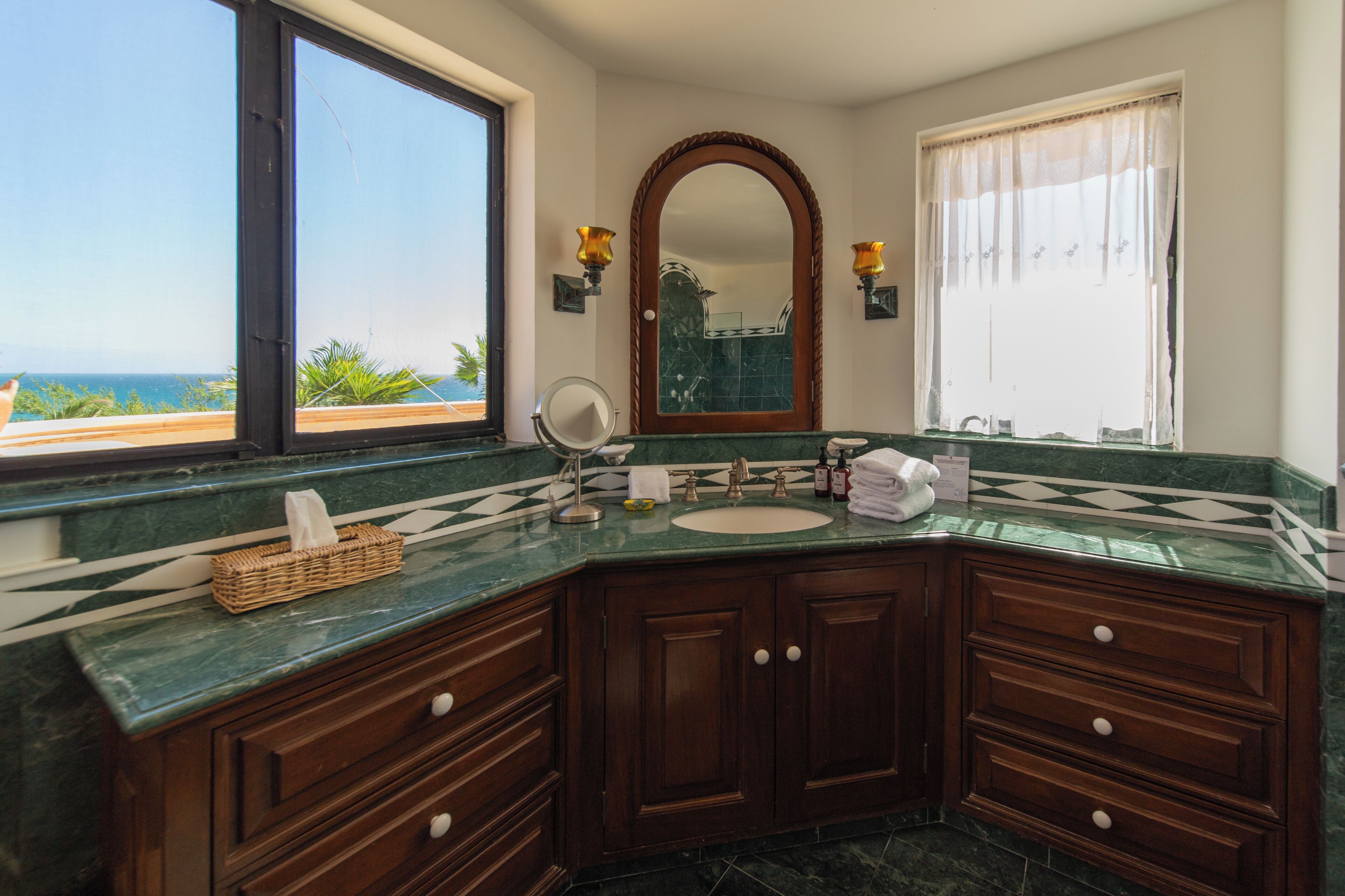 A bathroom with a large window, a mirror, a sink, and wooden cabinets.