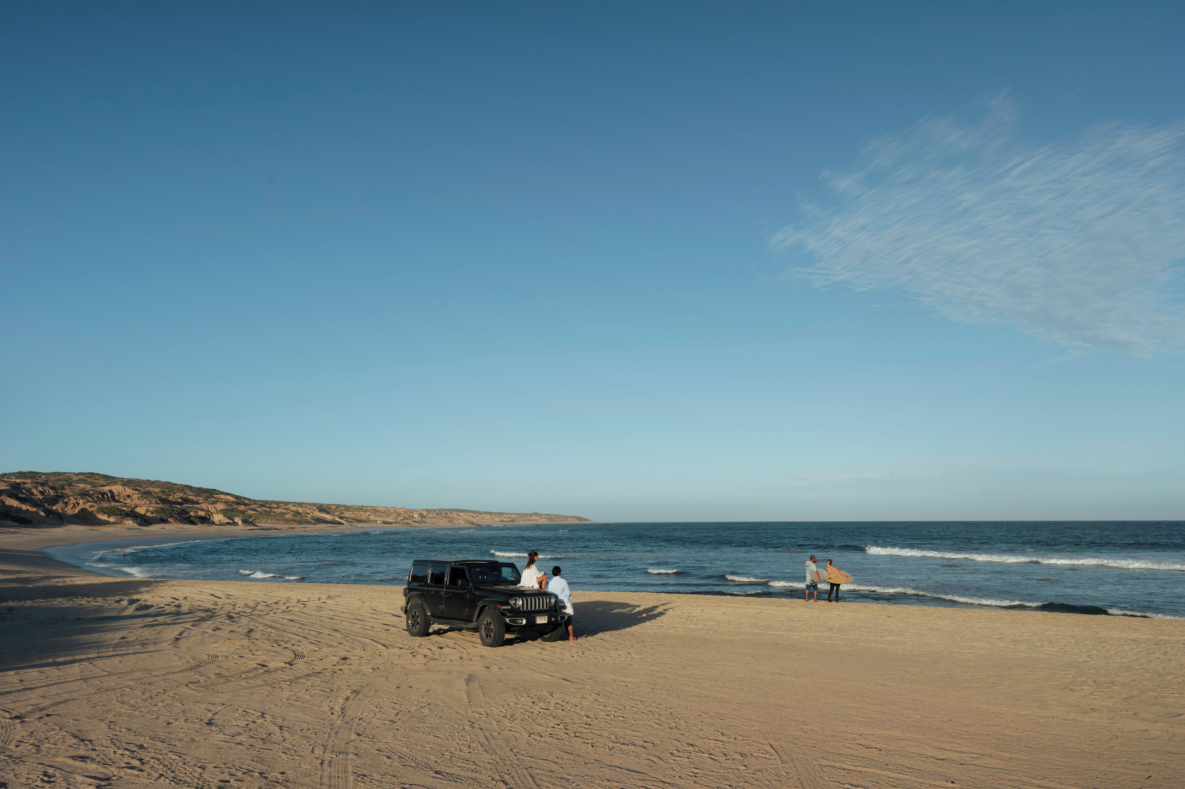 En strand med en sandbuggy parkeret i sandet, en klar himmel og havet i baggrunden.