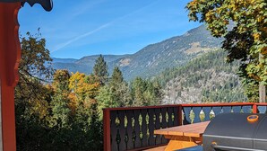 A patio with a grill, a wooden table, and a view of mountains.
