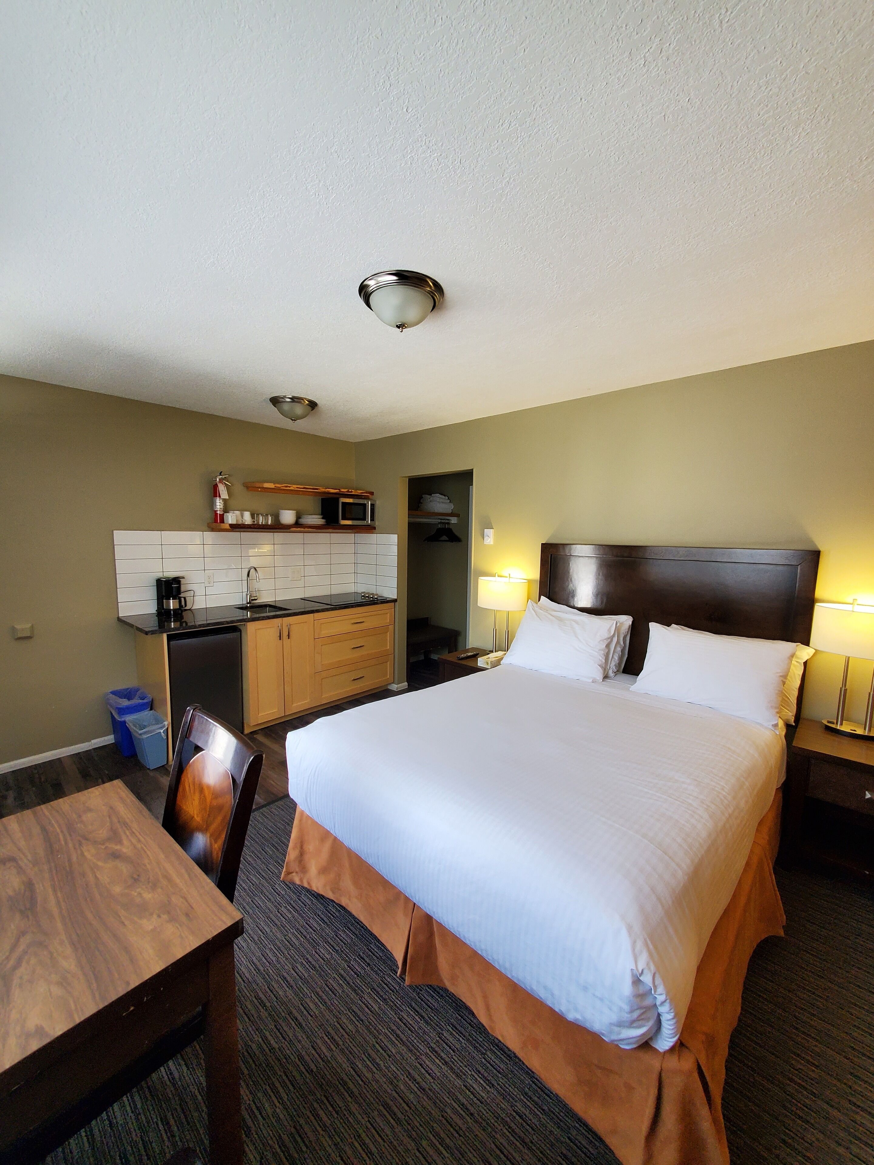 A hotel room with a large bed, a desk, a chair, a microwave, a sink, and a closet.