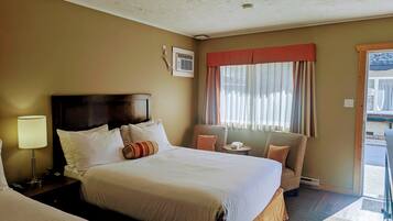A hotel room with a large bed, a bedside table with a lamp, a chair, a window with curtains, and a view of the outside.