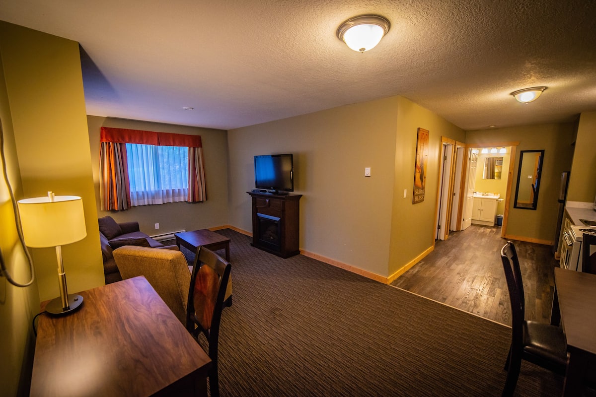 A hotel room with a TV, a dining table, a sofa, and a lamp.