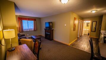 A hotel room with a TV, a dining table, a sofa, and a lamp.