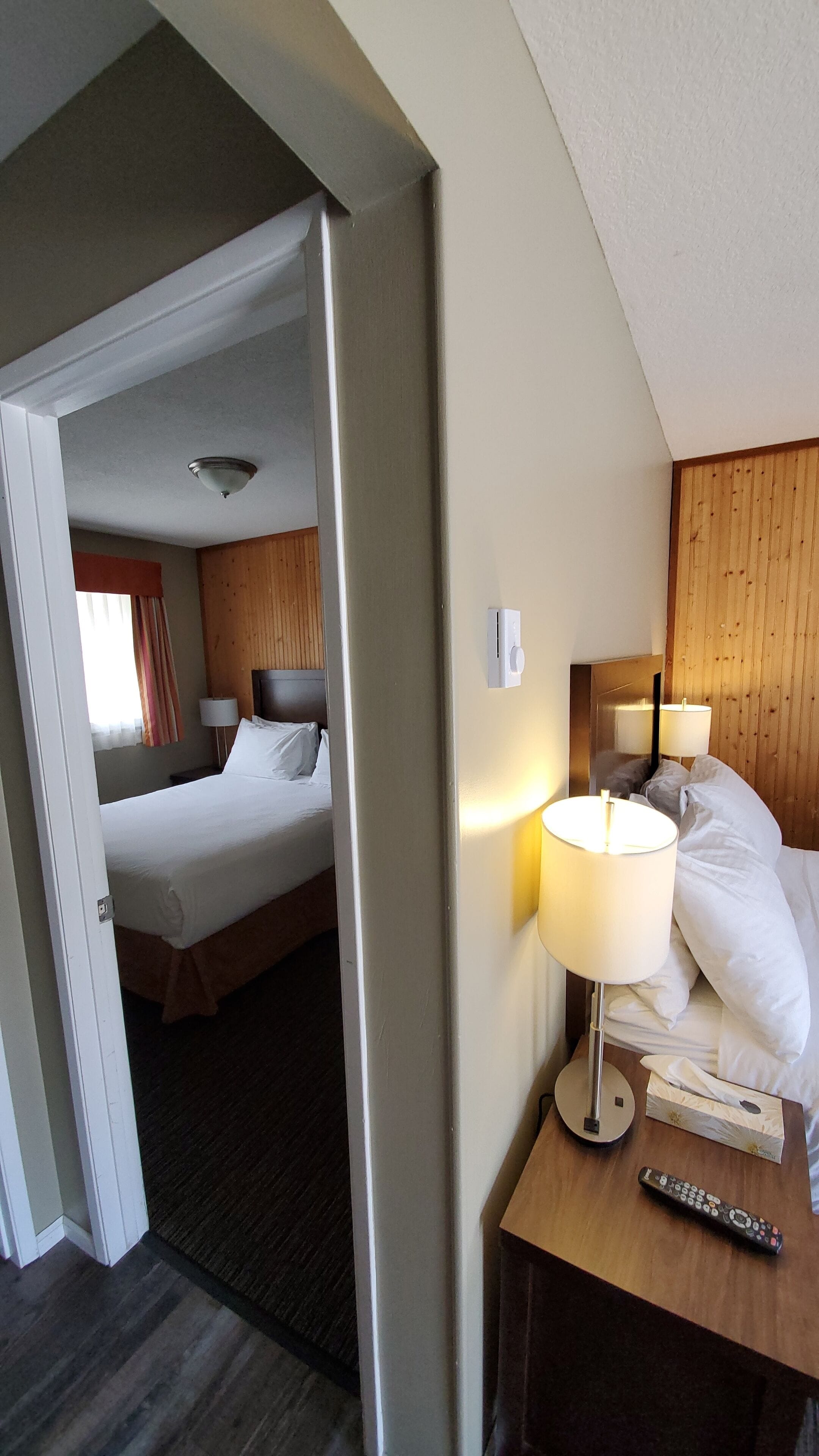 A hotel room with a bed, bedside lamps, a remote control, and a wooden headboard.