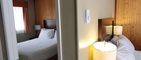 A hotel room with a bed, bedside lamps, a remote control, and a wooden headboard.