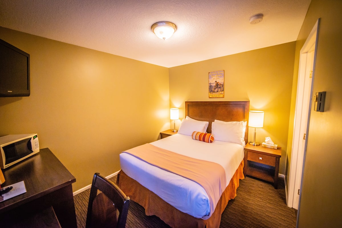 A hotel room with a bed, bedside lamps, a nightstand, a microwave, and a chair.
