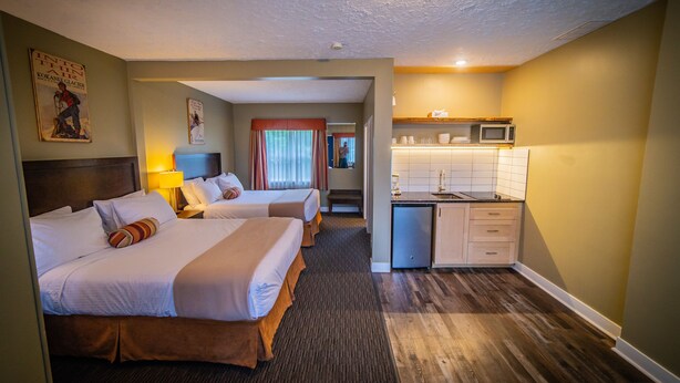 A hotel room with two beds, a kitchenette, and a bathroom visible in the background.