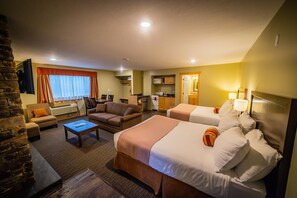 A hotel room with two beds, a sofa, a coffee table, and a kitchen area.