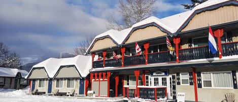 A row of snow-covered buildings with red railings and flags, indicating a winter resort setting.