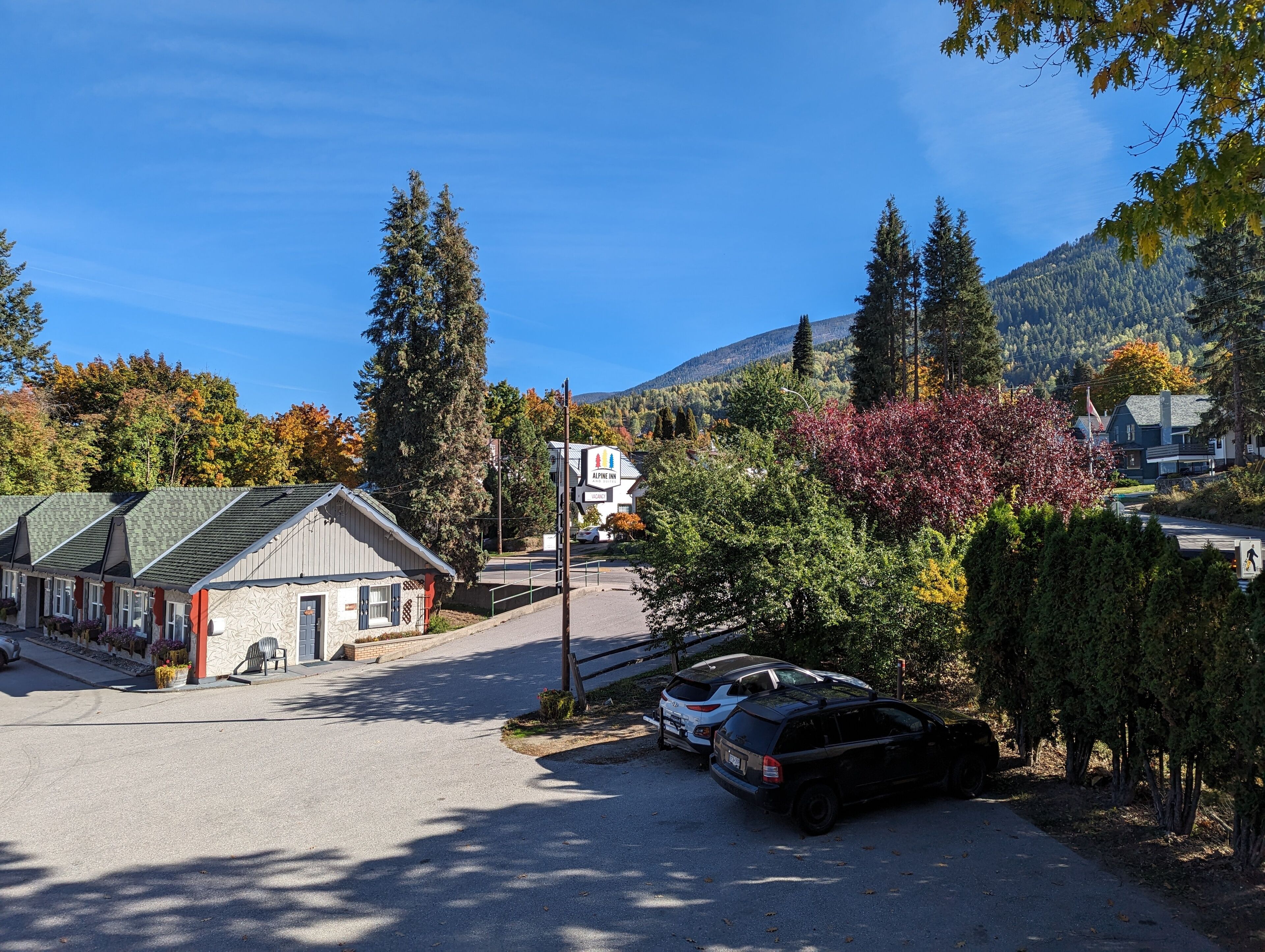A small town with a row of single-story buildings, including a hotel with a sign. There are parked cars and a clear sky.