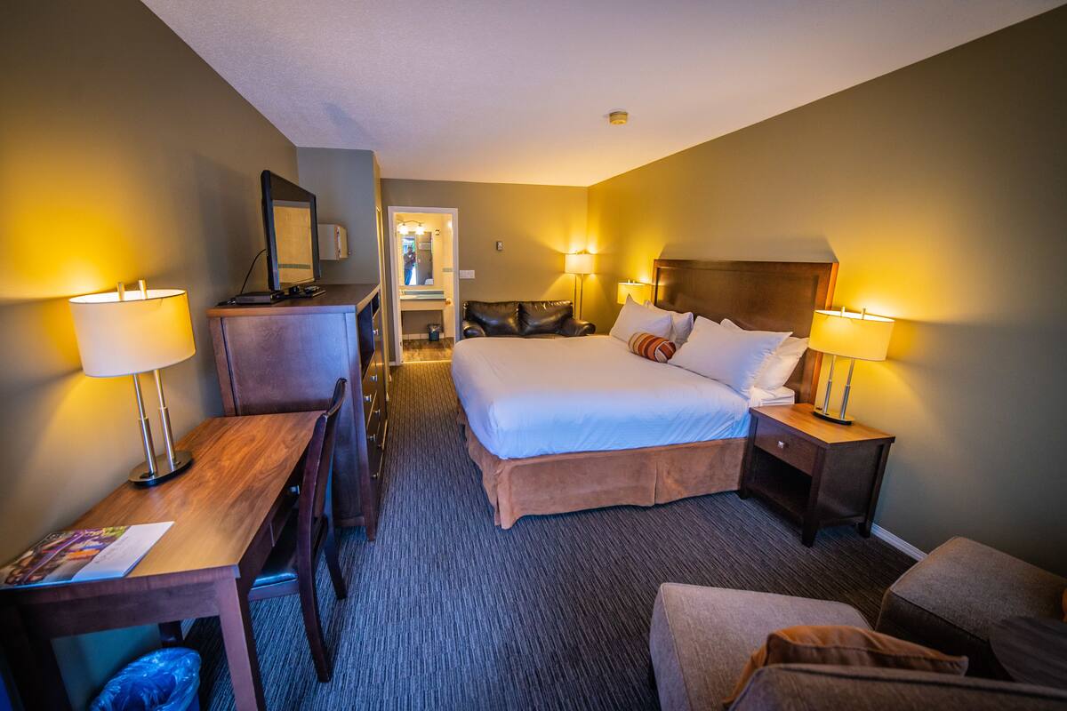 A hotel room with a bed, two bedside tables with lamps, a desk, a chair, and a trash bin.