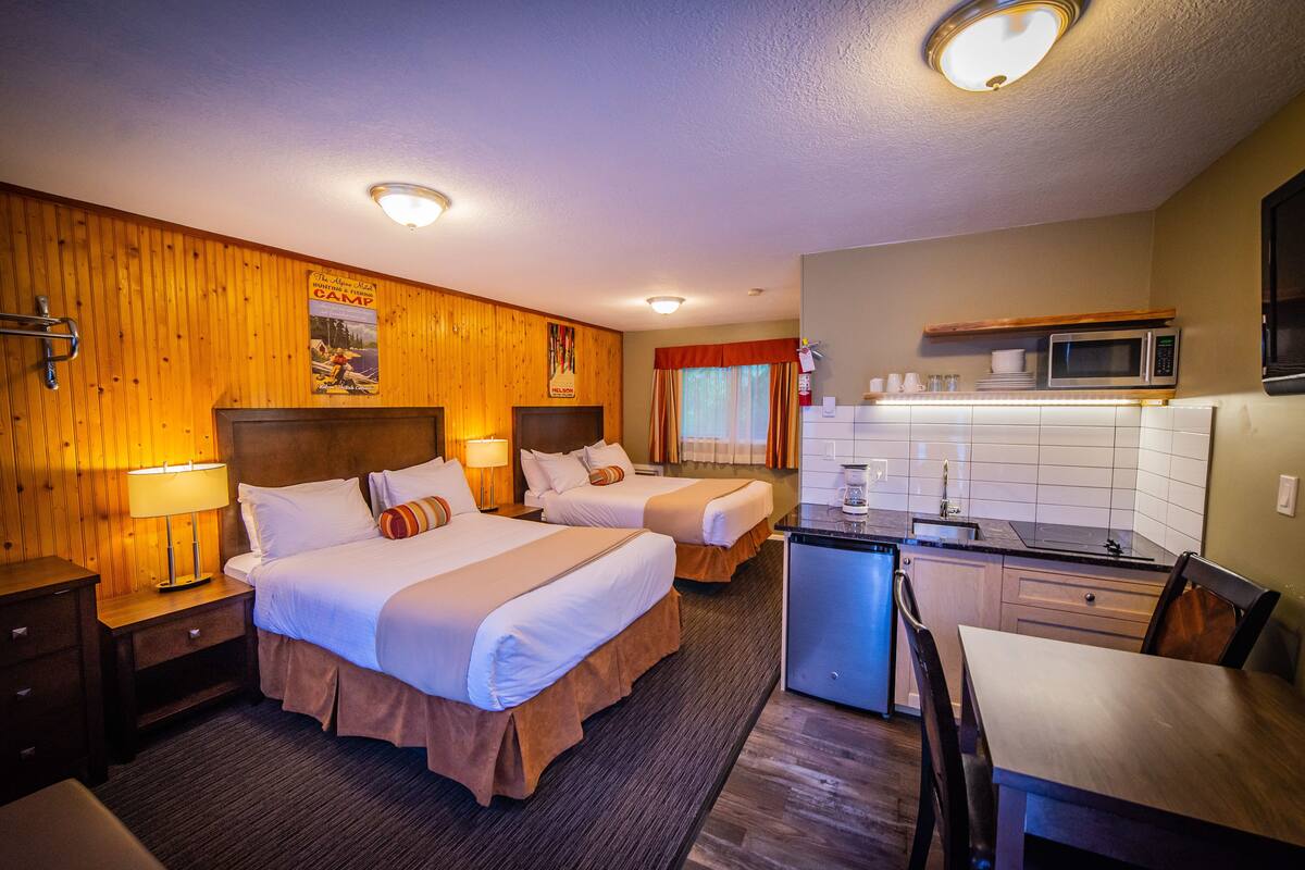 A hotel room with two beds, a kitchenette, and a dining area.