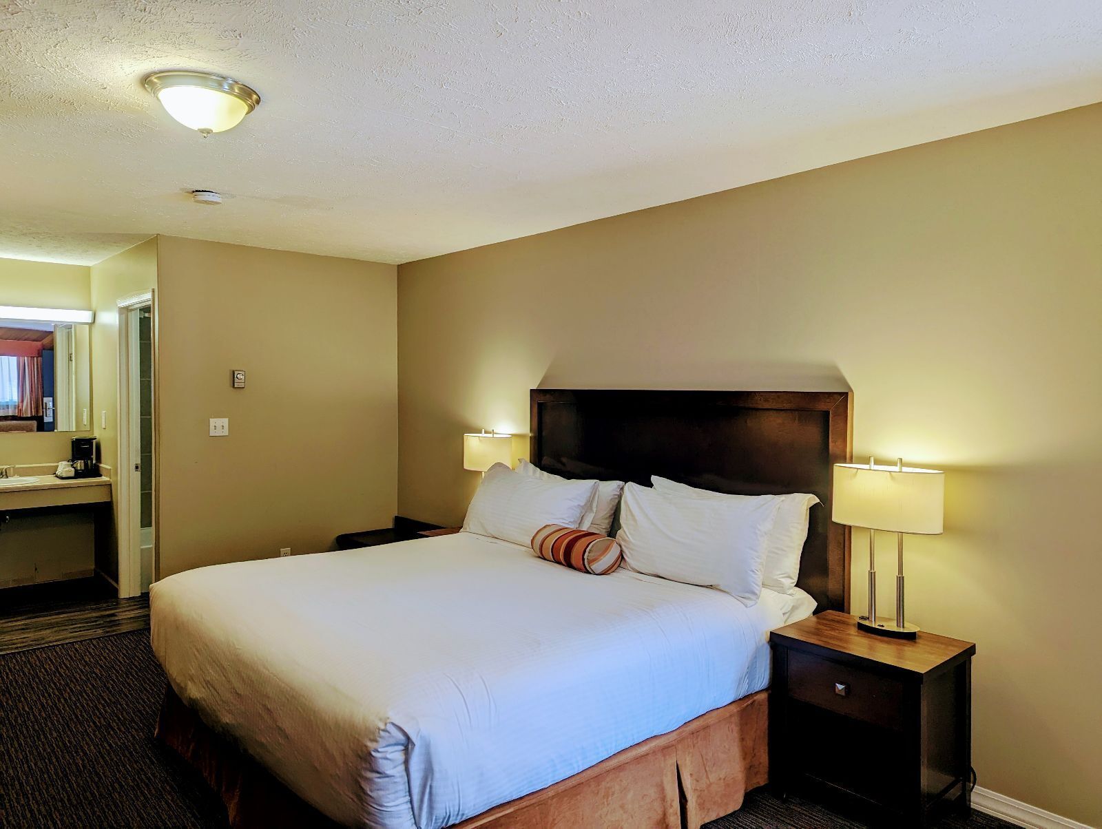 Une chambre d’hôtel avec un grand lit, des lampes de chevet, une tête de lit en bois et un petit bureau avec une lampe.