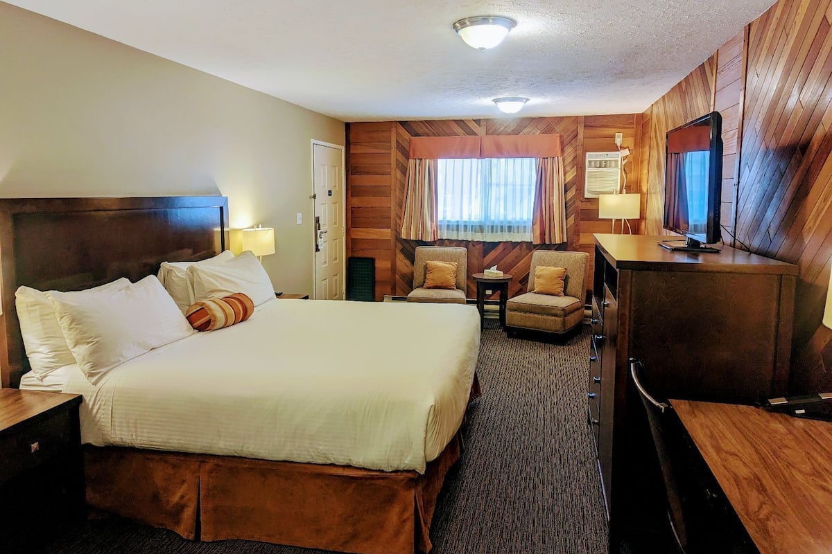 A hotel room with a large bed, two armchairs, a desk with a television, and a wooden wall paneling.