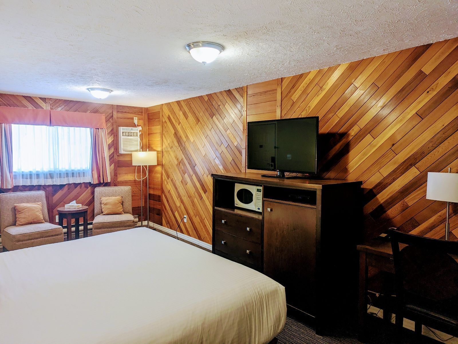 A hotel room with a bed, two armchairs, a TV, a microwave, and a desk.