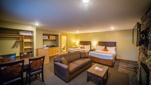 A hotel room with a sofa, two beds, a dining area, and a kitchen.