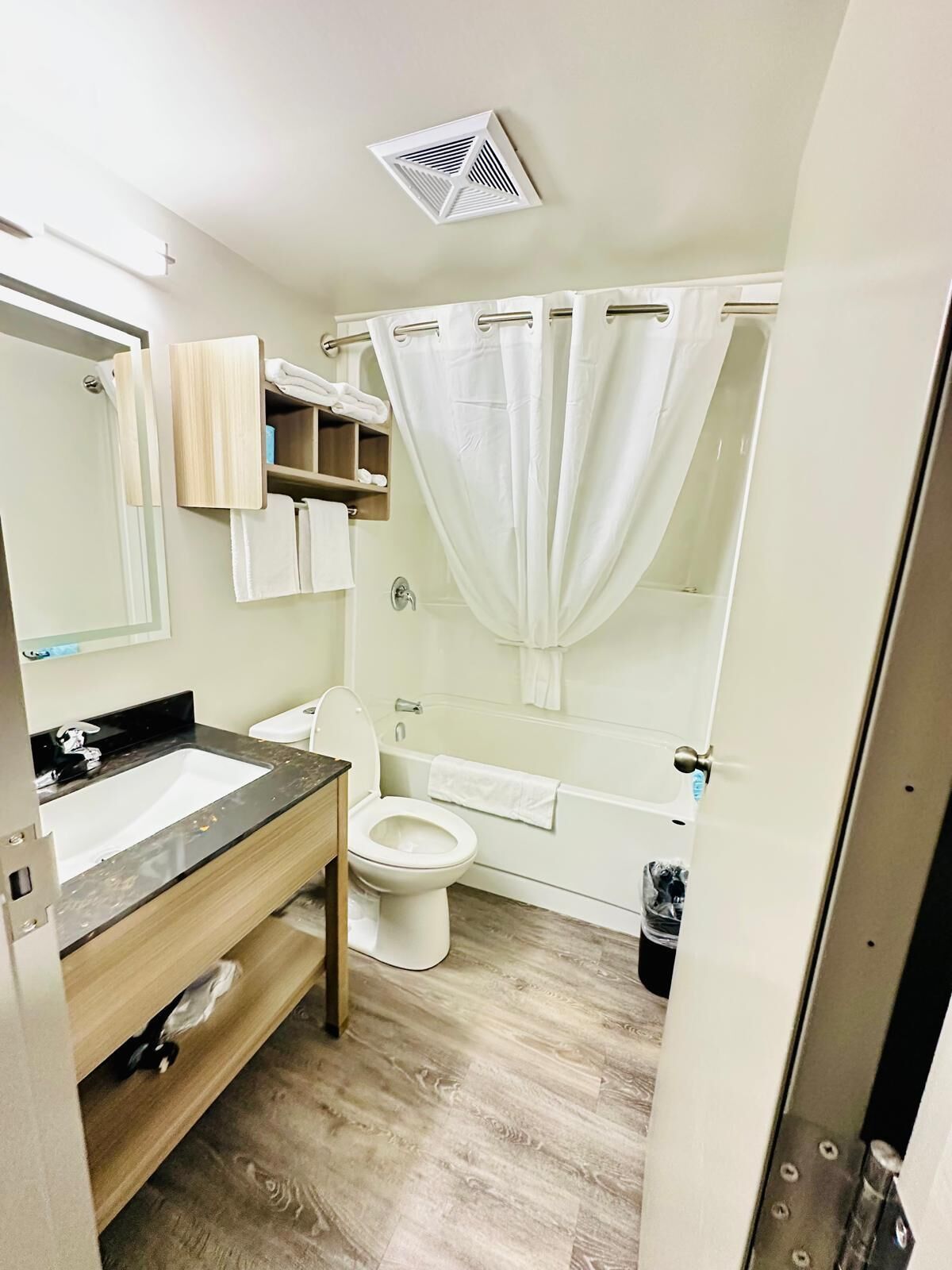 Une salle de bain avec un lavabo, des toilettes et une baignoire. On y trouve un rideau de douche et un porte-serviettes.