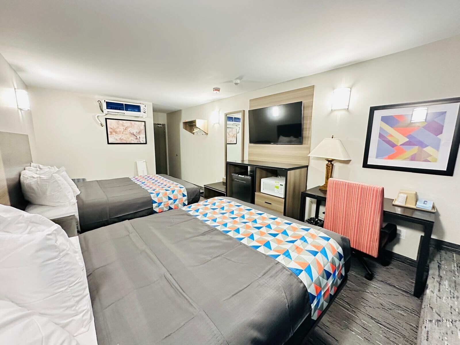 Habitación de hotel con dos camas, televisor, escritorio y lámpara.