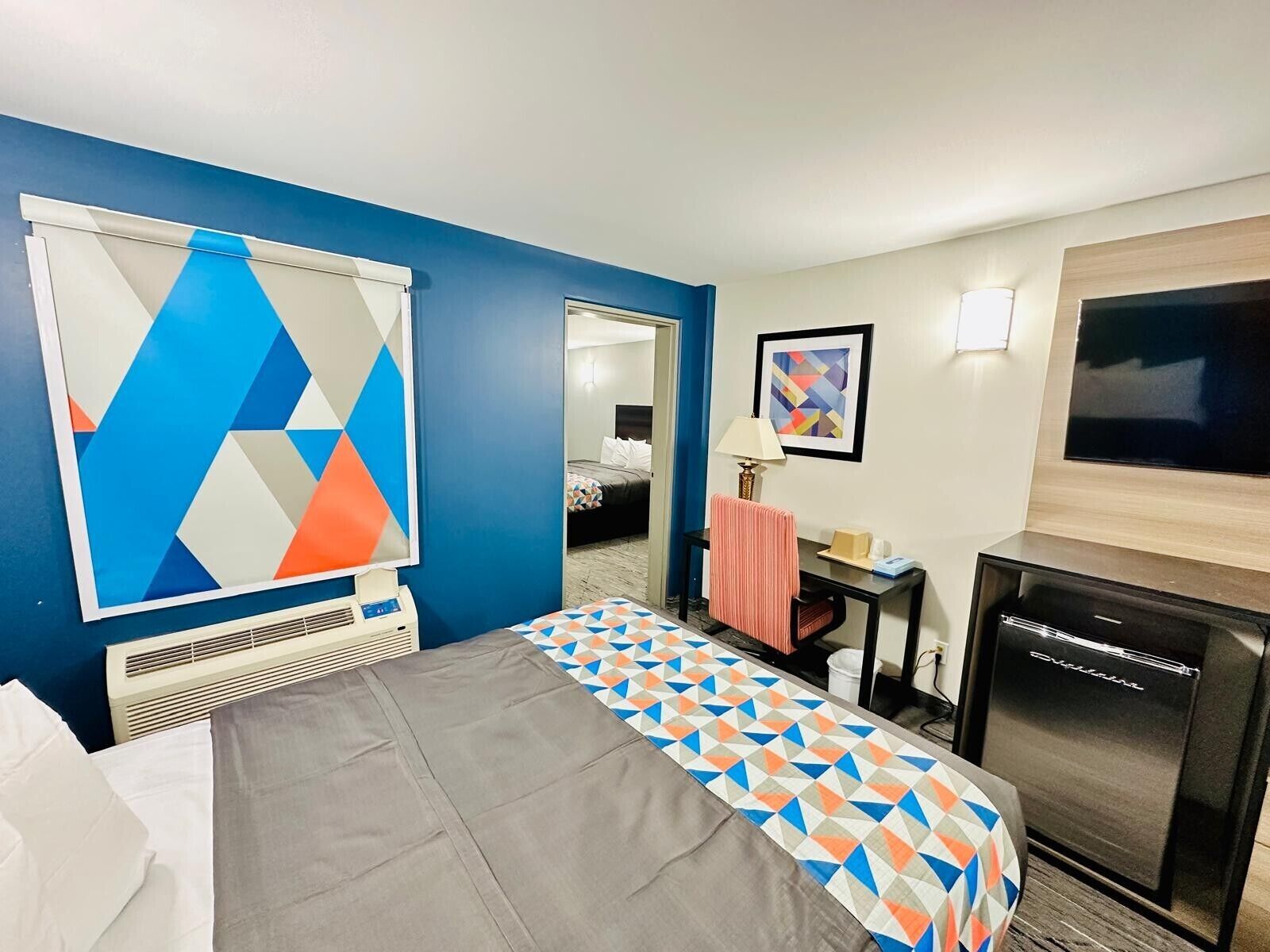A hotel room with a bed, a desk, a chair, a television, and a large window.