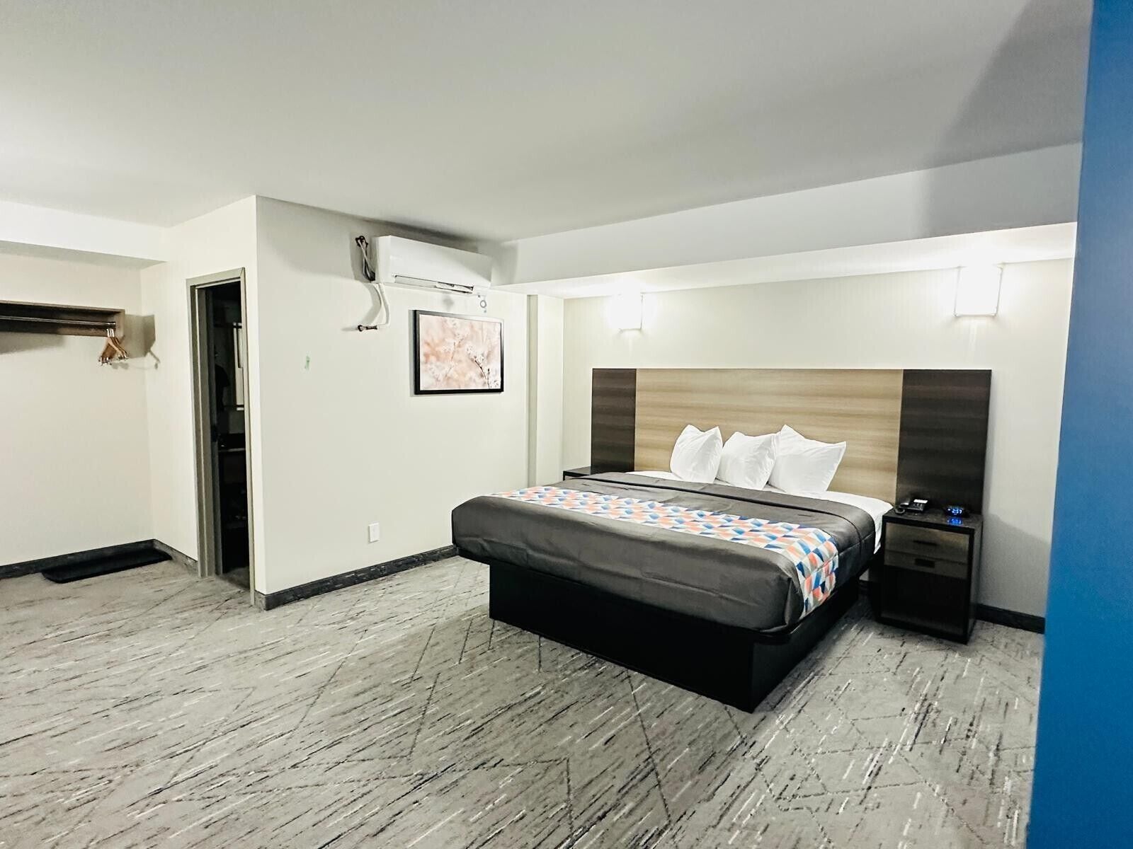 Habitación de hotel con cama, mesita de noche y aire acondicionado instalado en la pared.