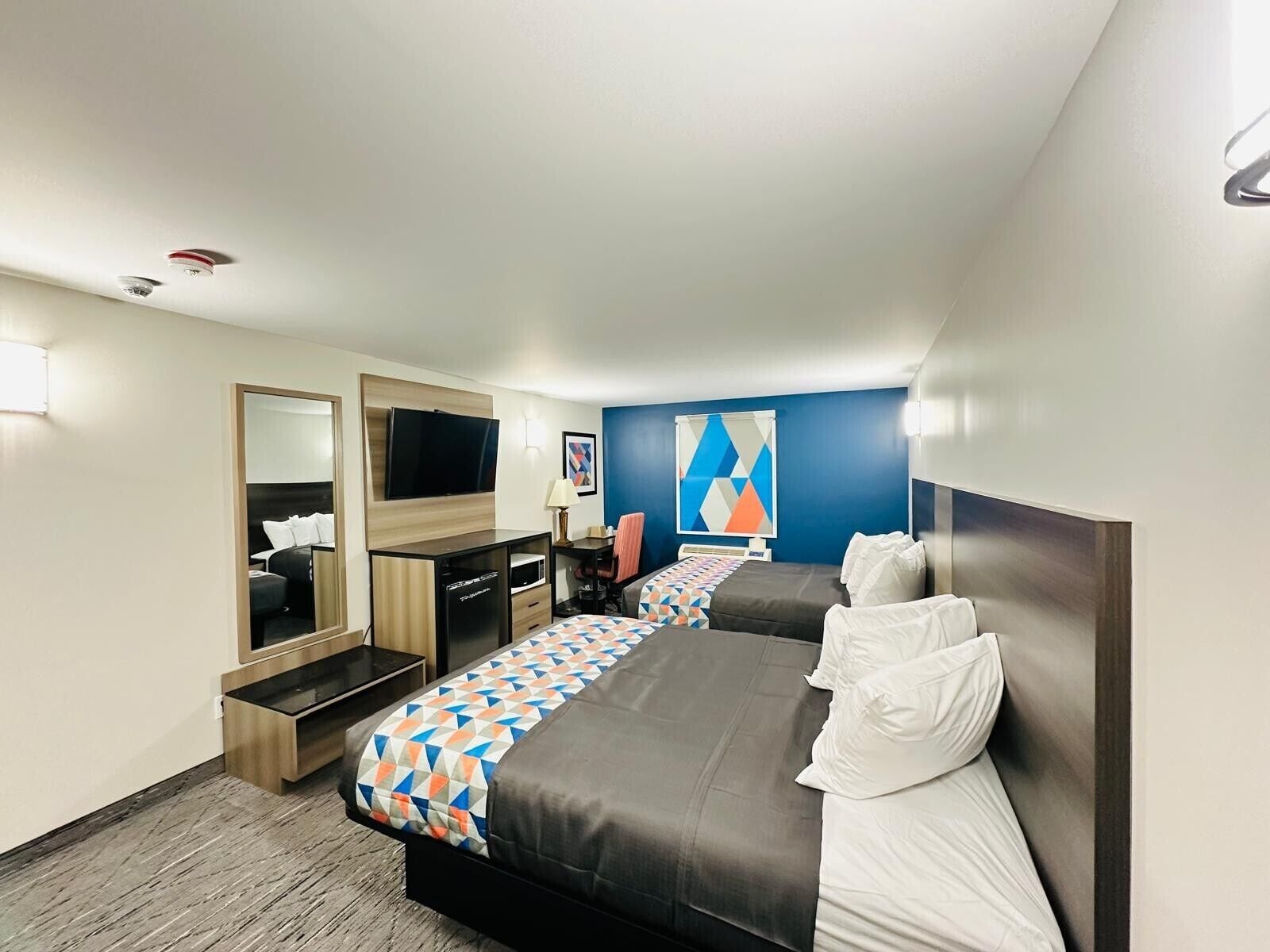 A hotel room with two beds, a desk, a chair, a TV, and a large mirror.