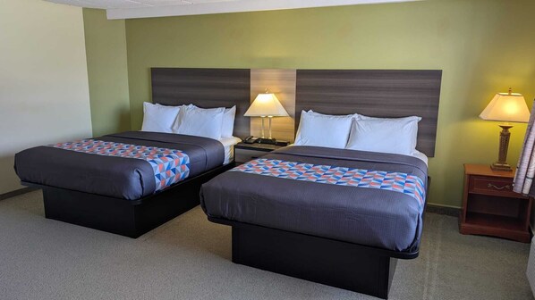 A hotel room with two beds, each with a patterned bedspread and pillows, a nightstand with a lamp, and a wooden nightstand with a lamp.