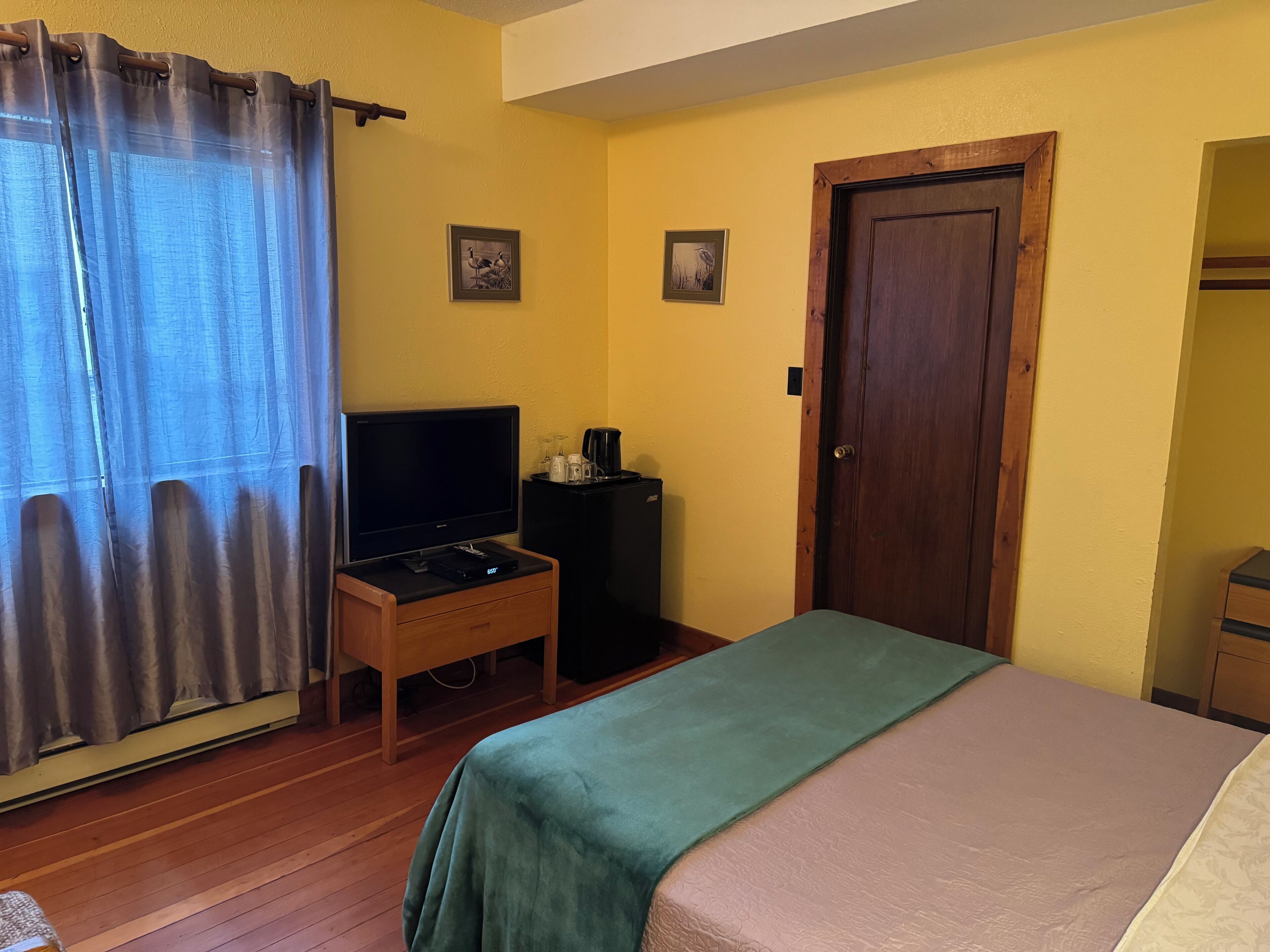 Una habitación con una cama, un televisor sobre un mueble bajo, una puerta y dos cuadros en la pared.