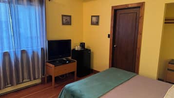 Una habitación con una cama, un televisor sobre un mueble bajo, una puerta y dos cuadros en la pared.