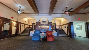A hotel lobby with a grand staircase, a reception desk, and a seating area with two chairs. - Rodmay Heritage Hotel (Powell River)