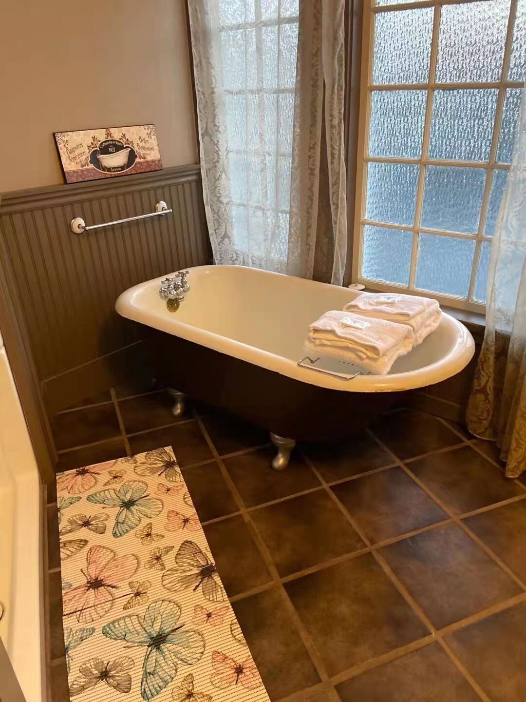 A bathroom with a clawfoot bathtub, a towel rack, and a window with curtains.