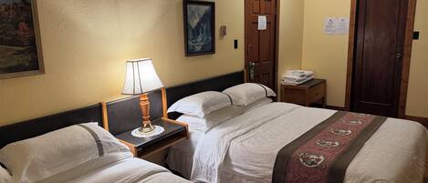 A hotel room with two beds, a nightstand with a lamp, a framed picture on the wall, and a door with a sign.