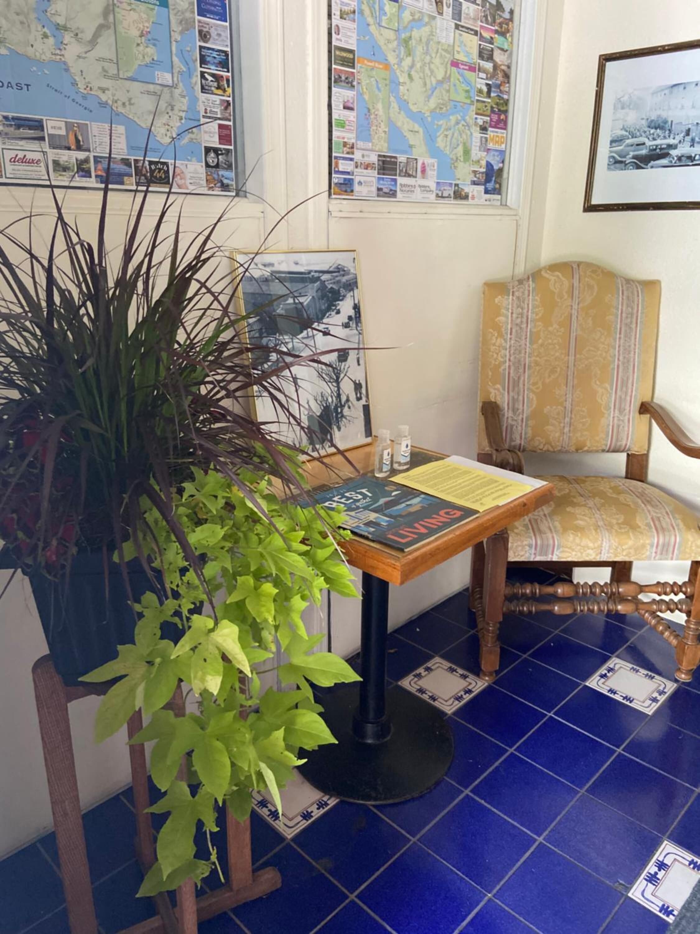 Una habitación con un mapa en la pared, una silla de madera, una mesa con un libro y una planta en maceta.