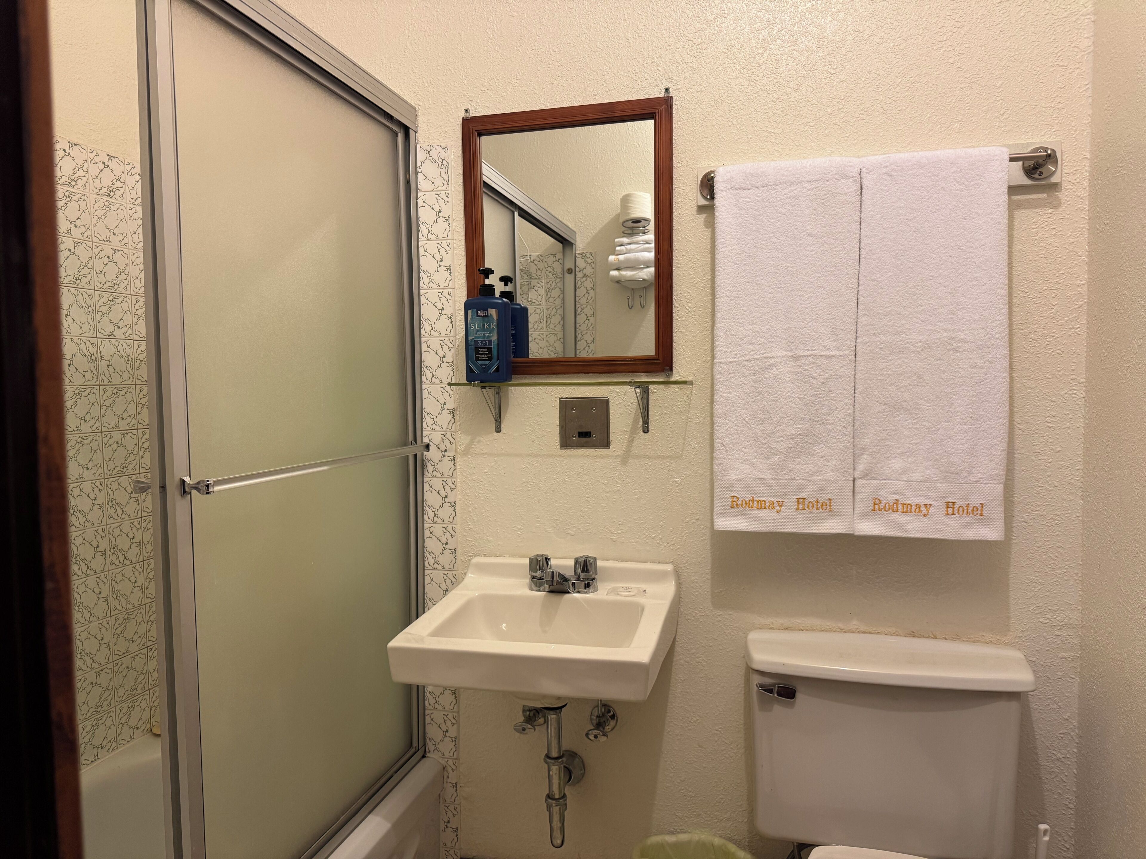 A bathroom with a glass shower door, a sink, a toilet, a mirror, and a towel rack with a towel.