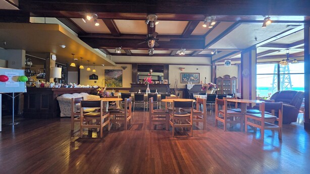 A restaurant with wooden tables and chairs, a bar area, and a view of the ocean. - Rodmay Heritage Hotel (Powell River)