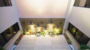 Een moderne binnenplaats met een houten terras, planten in potten en ingebouwde planters langs de muren.