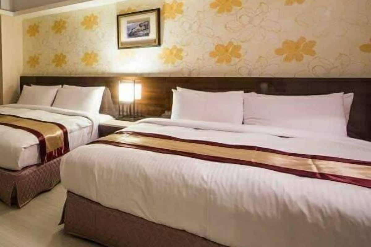Une chambre d’hôtel avec deux lits, chacun agrémenté de draps blancs et d’un élément décoratif marron. Un tableau encadré est accroché au mur au-dessus des lits.